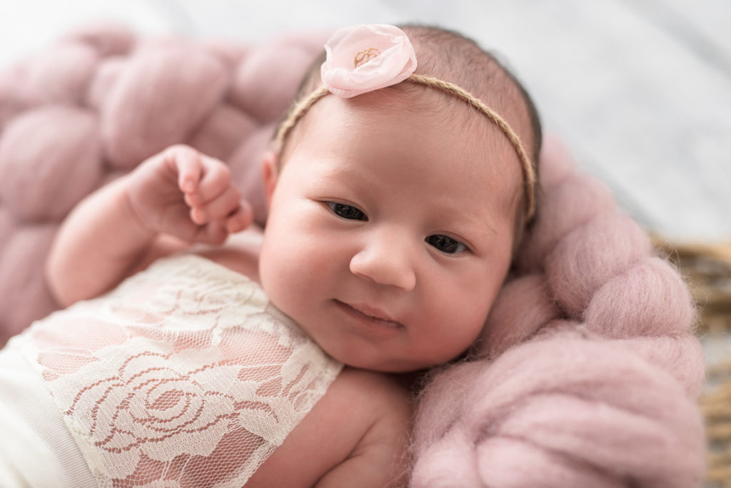 Smiling newborn posed in pink basket in Waxhaw home