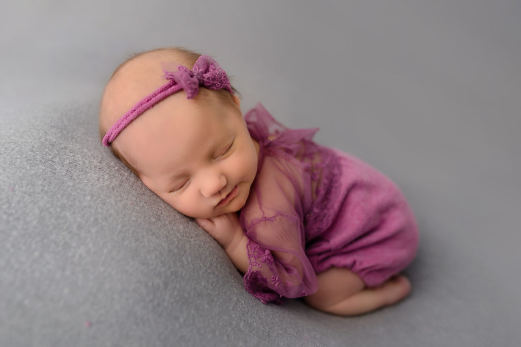 Smiling baby in maroon outfit with matching bow studio photography