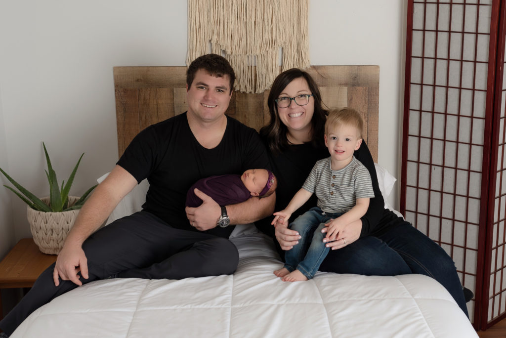 Family picture all smiles in lifestyle bed in studio with new baby girl