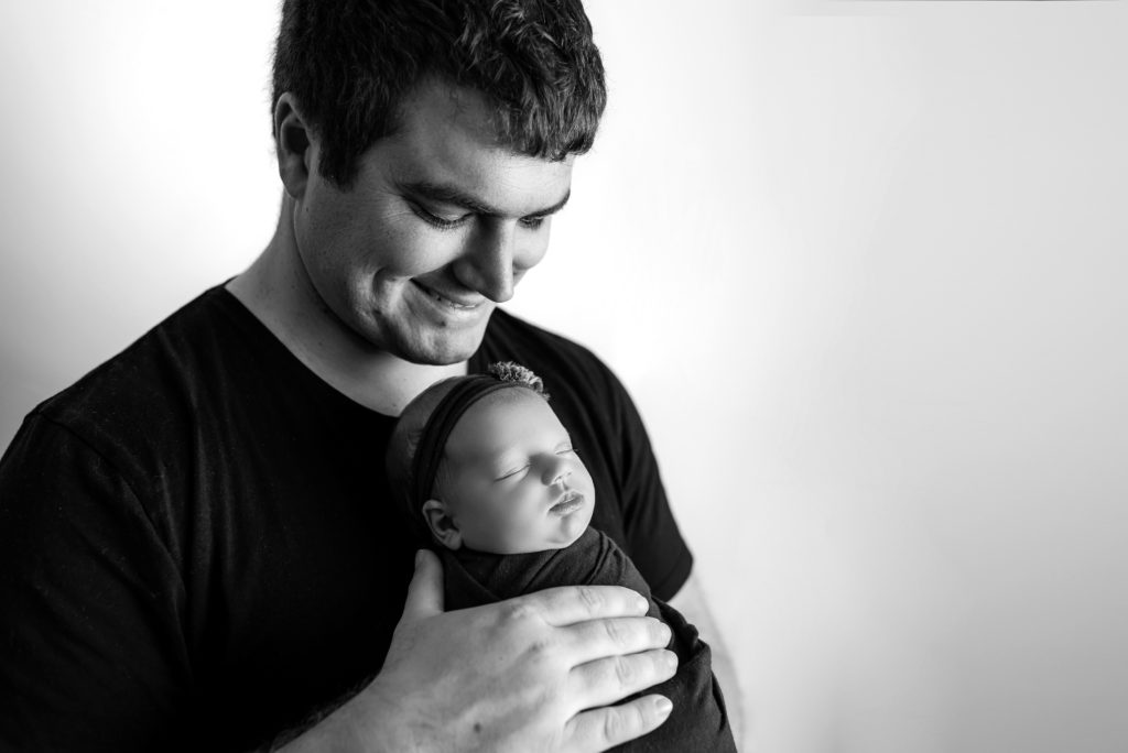 Black and white photo of dad smiling down at baby girl in hands close up
