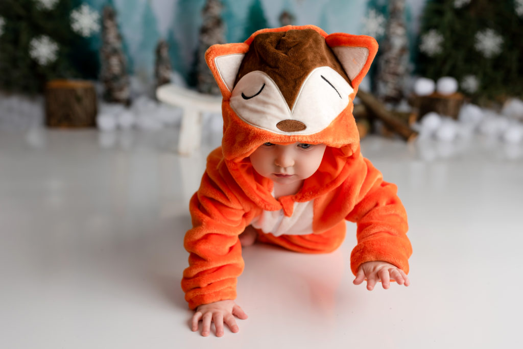 Child in orange fox outfit crawling away on photography winter set