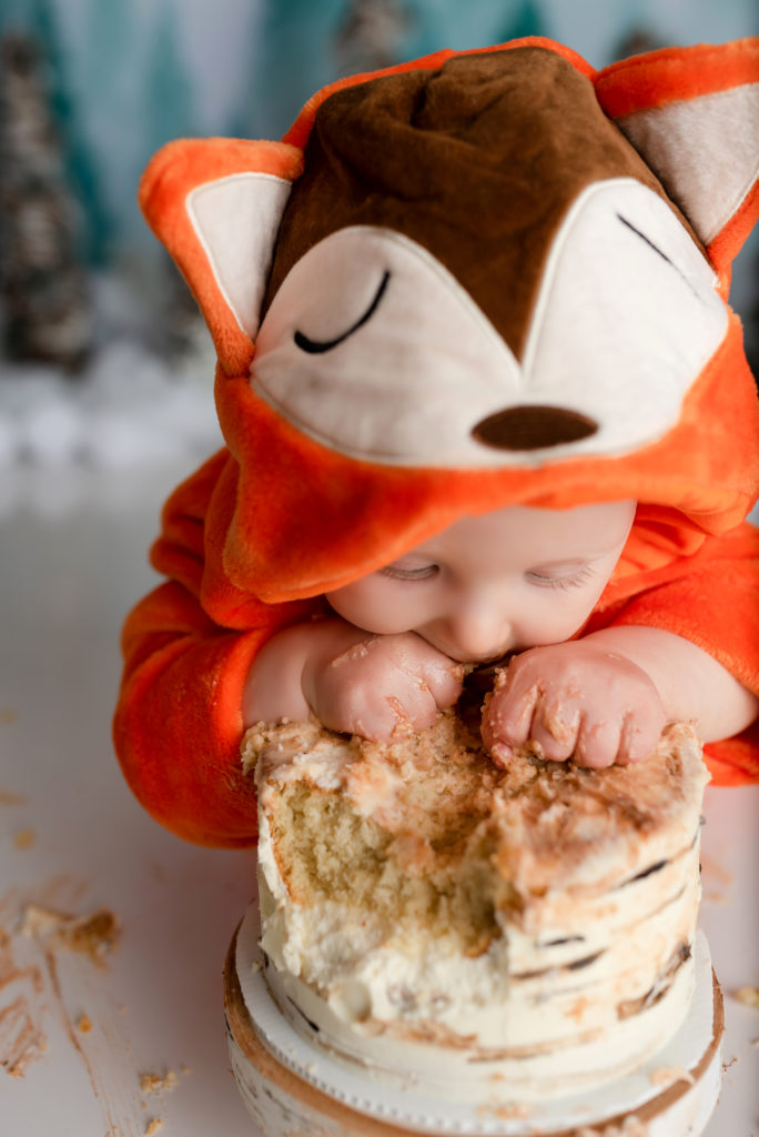 Baby boy with fox hood diving into smash cake for first birthday photography