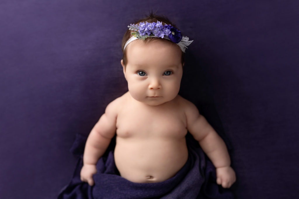 Purple backdrop and flowers with baby for milestone newborn session