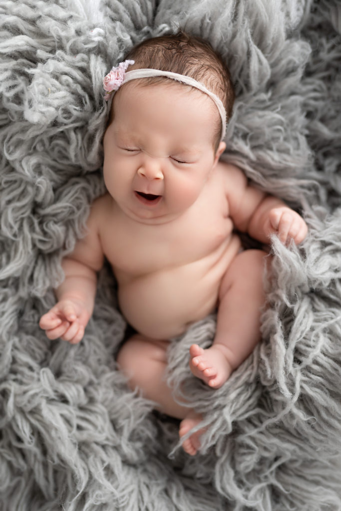 newborn baby yawning in gray fluff in the nude
