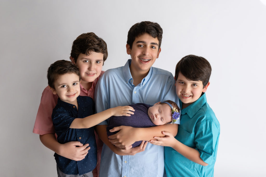 Brothers smiling at camera holding newborn sister in studio