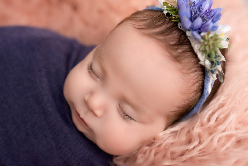 Purple baby wrapped with headband on pink fluff sleeping close eyes
