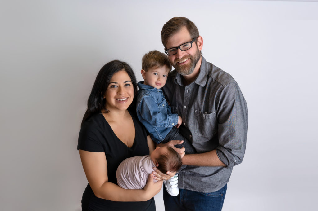 family portrait with newborn girl mom dad and brother on white