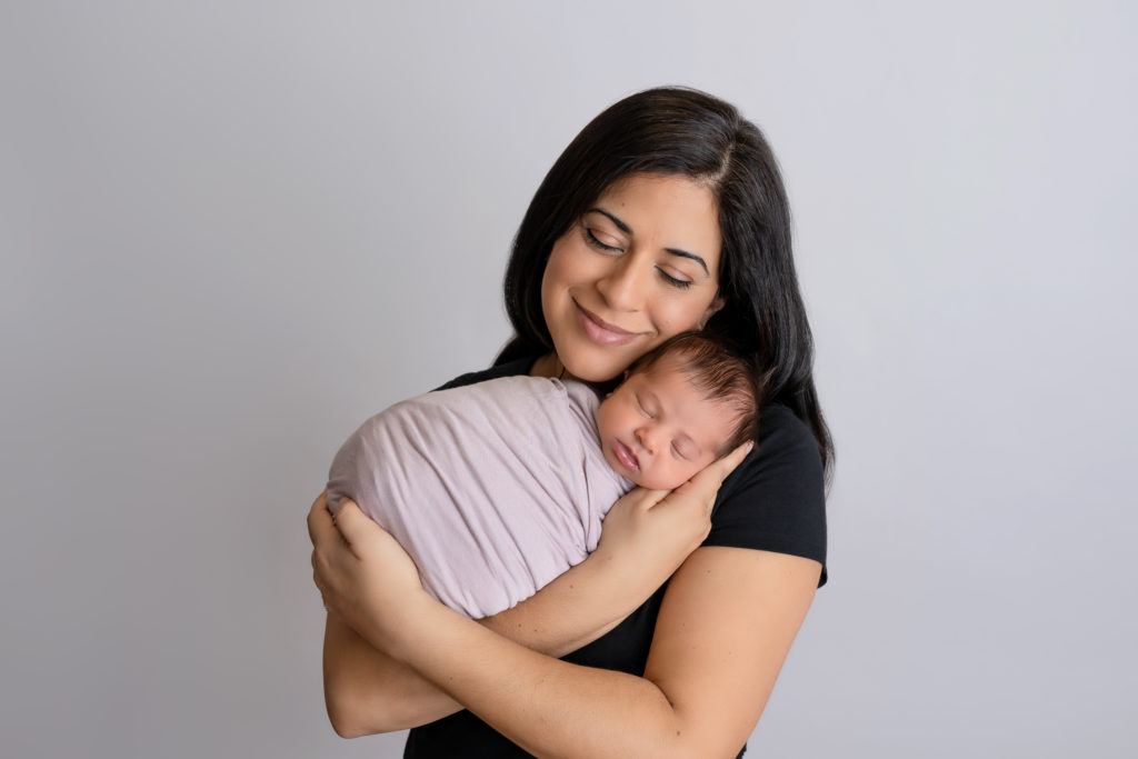 mama snuggles her newborn baby girl in arms on white