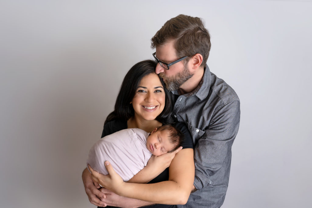 Dad giving mom a kiss with their newborn girl in moms arms newborn session photo