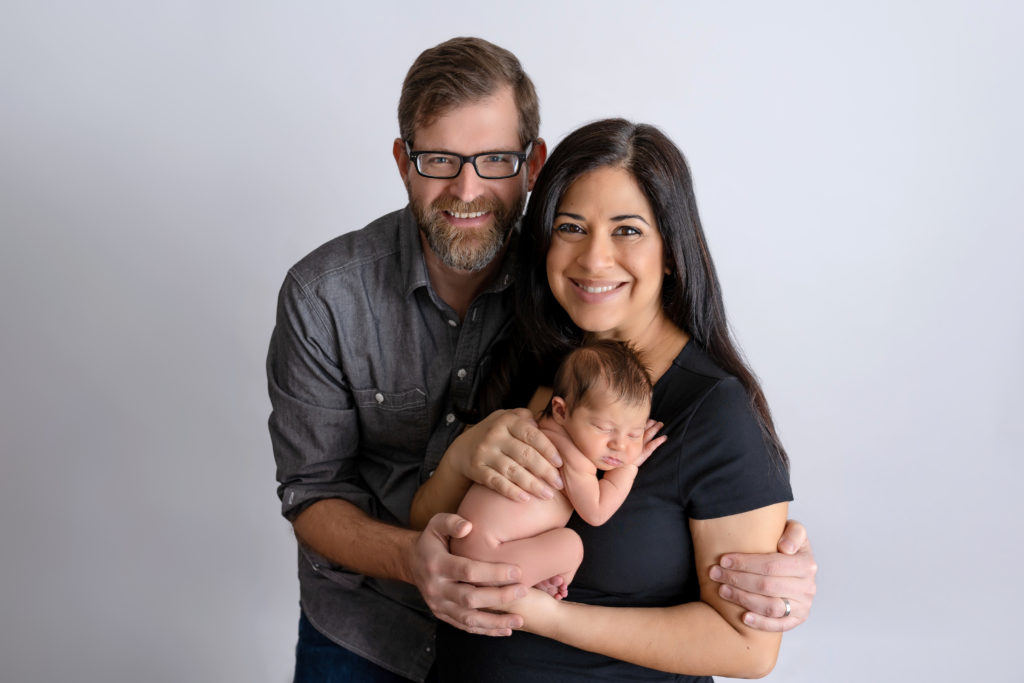 Mom and Dad with nude baby girl posing on parents newborn photographer