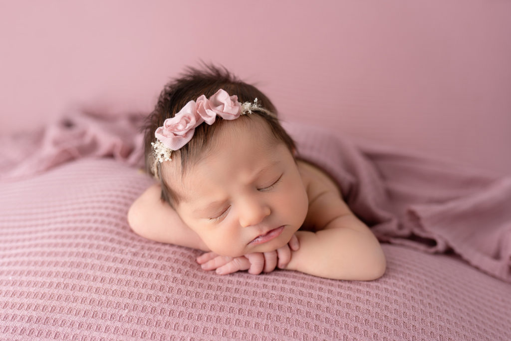 Baby girl in pink with floral headband chin on hands newborn posed