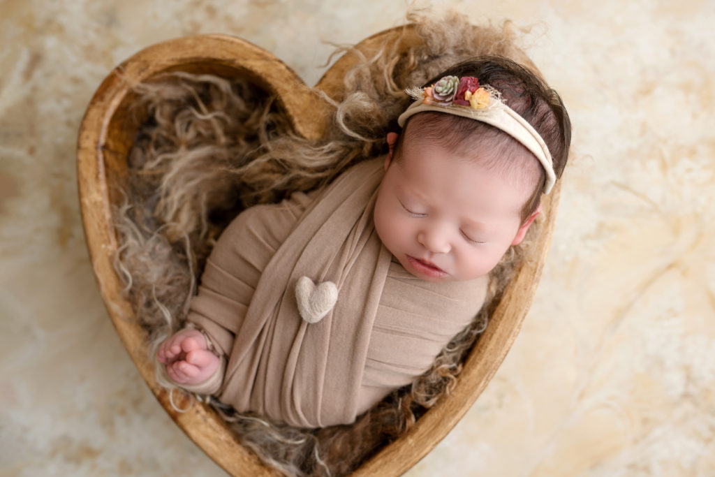 newborn baby girl in heart-shaped bowl in-studio