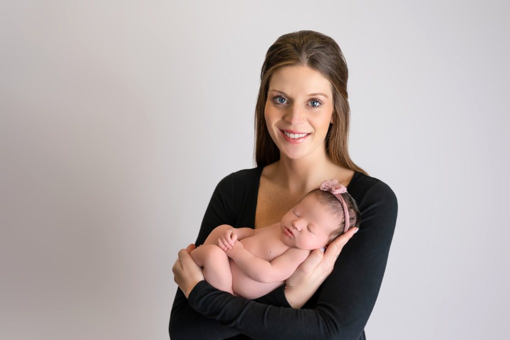 new mom posed on white backdrop with newborn baby