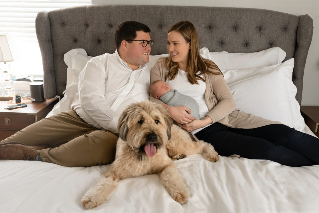 whole family look at one another with dog and newborn on bed in room 