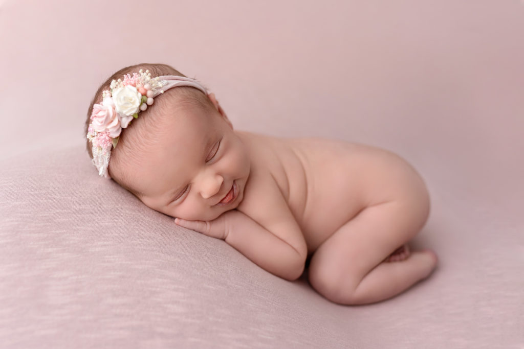 newborn baby bum asleep on hands on pink soft sheet