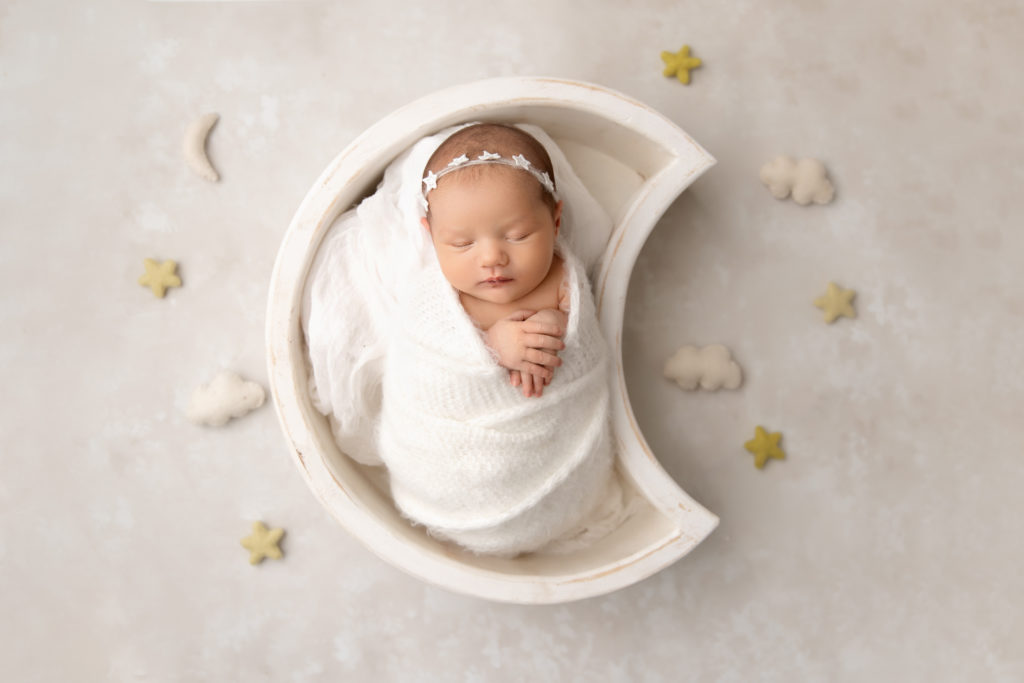 baby girl in white wrap in moon shaped bowl