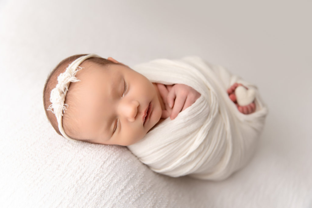 newborn sleeping in white wrap with heart between feet