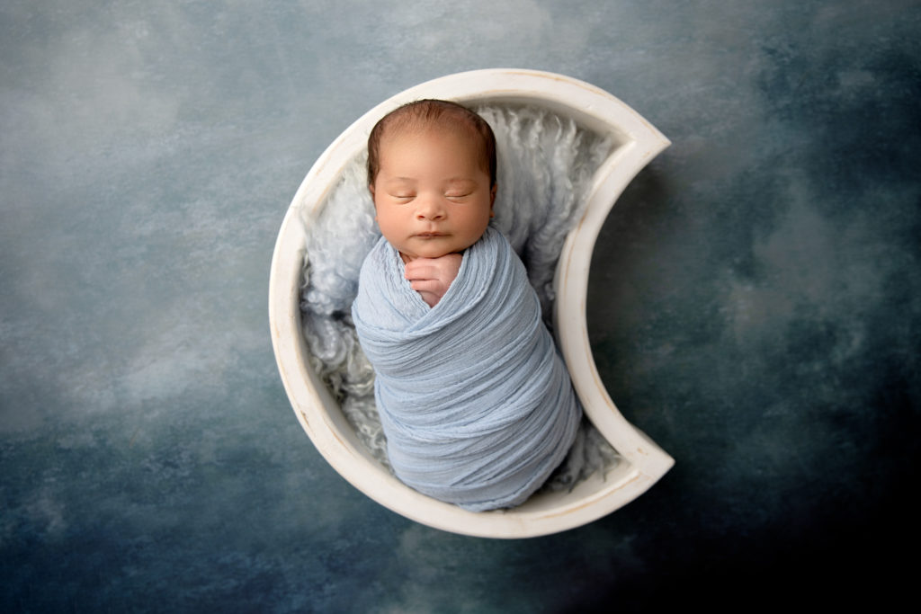 newborn in moon bowl with blue wrap and backdrop