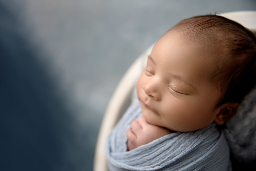 close up of newborn face with blue backdrop