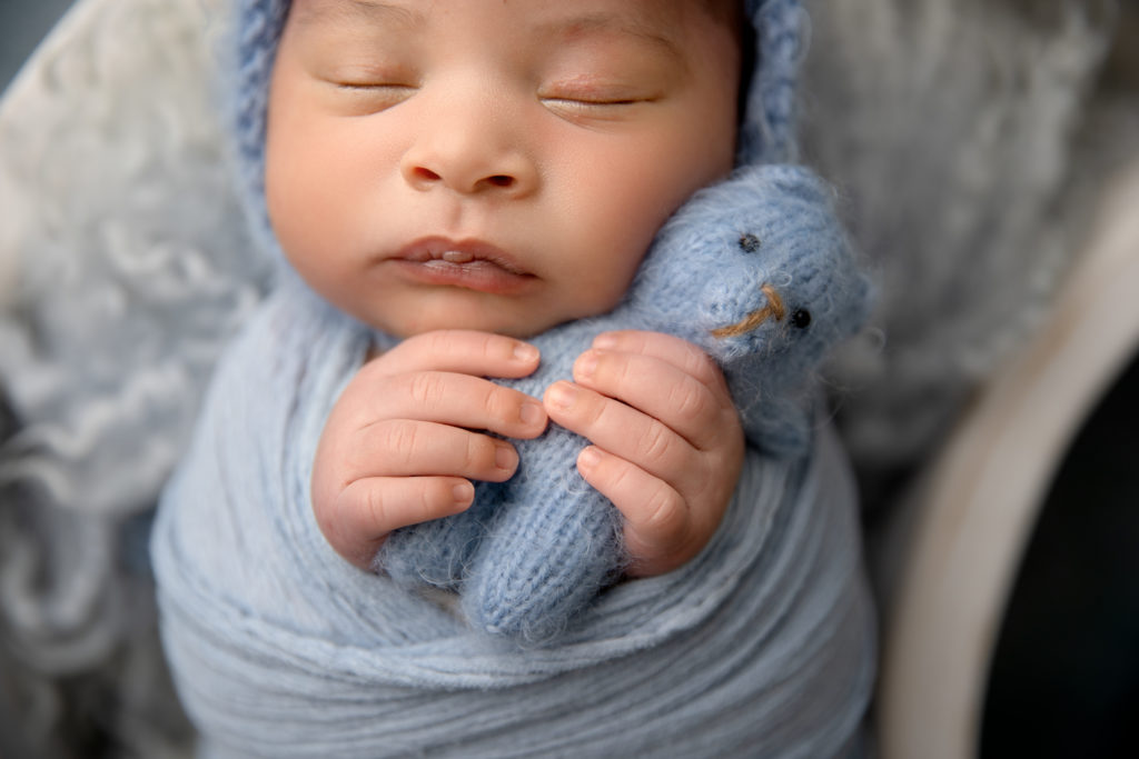 close up of newborn wrapped in blue holding tiny stuffed blue bear