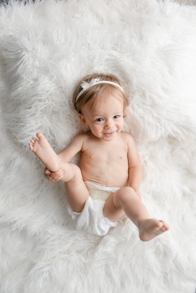 One year old baby photo on white blanket smiling 