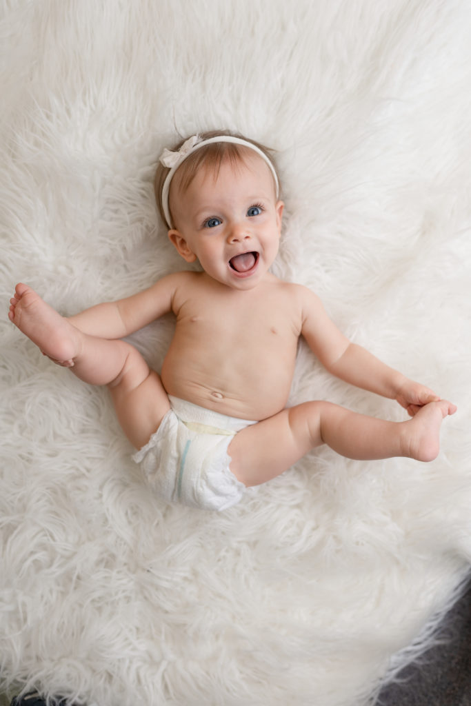 Happy baby kicking legs on white blanket baby portrait photography 