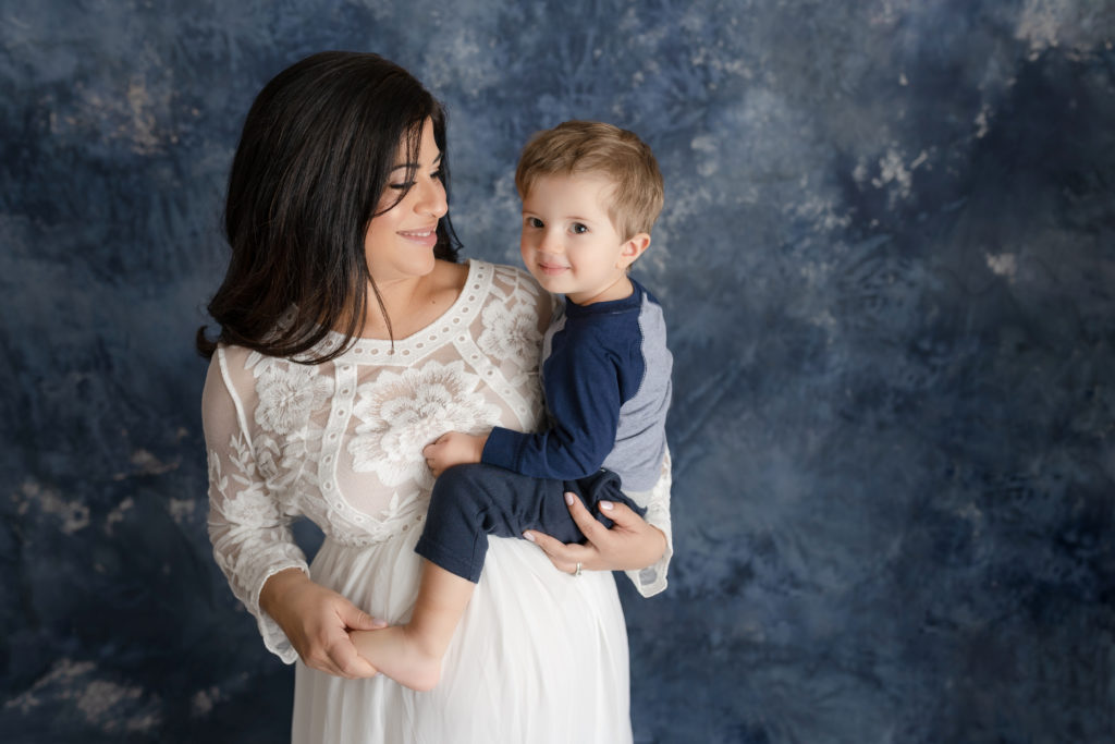 Pregnant mama looking at son in arms in studio maternity portrait 

