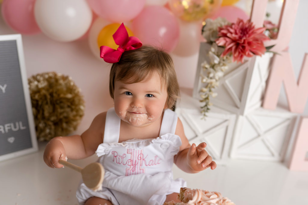 baby girl with pink bow smiling at camera during cake smash 