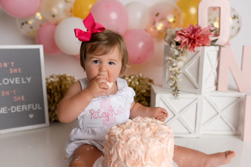 Child eating pink rosette cake for 1 year cake smash photo session
