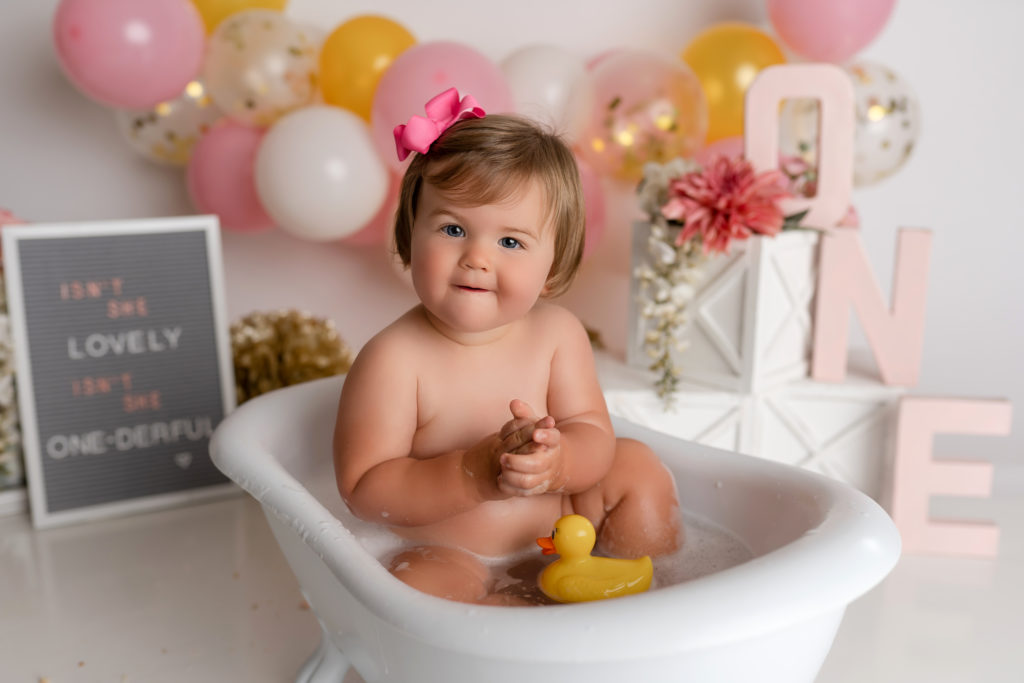 Little girl with rubber ducky in claw foot tub after cake smash