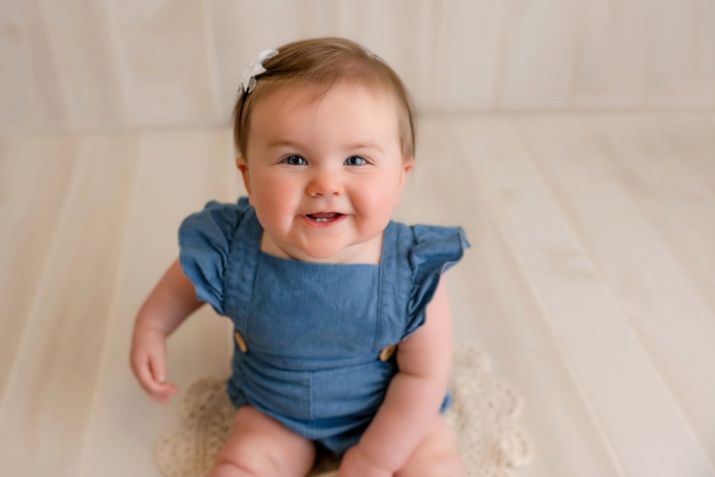 smiling baby girl on jean outfit in studio milestone session
