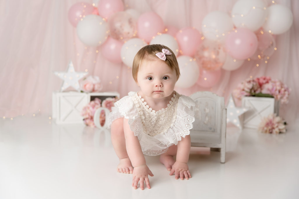 baby girl dressed in white for cake smash with pink balloons