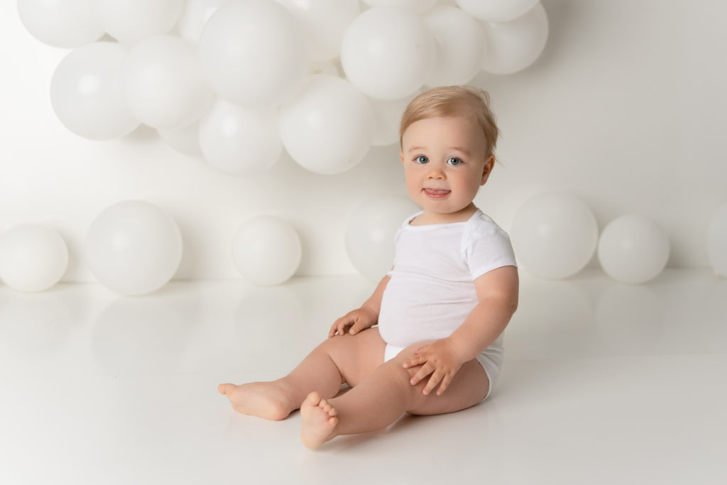 baby boy white onesie with white balloon backdrop