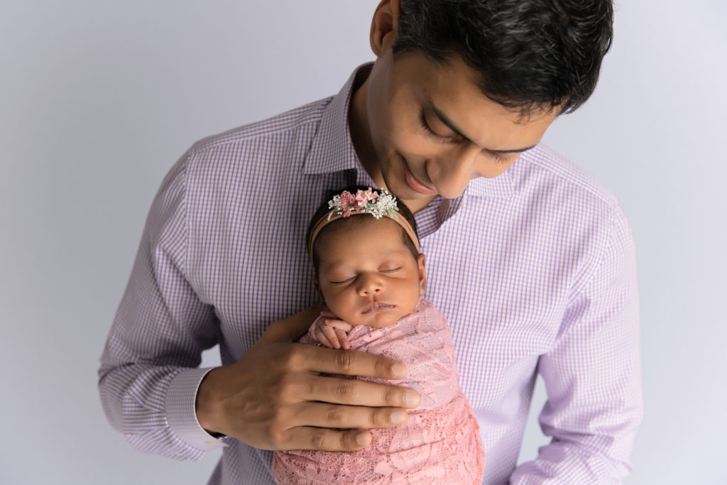father holding newborn girl wrapped in pink