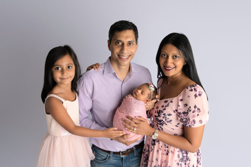 parents and sister pose with newborn girl wrapped in pink