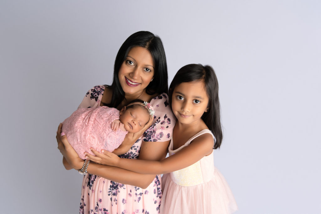 mother poses with daughter and newborn girl in matching pink