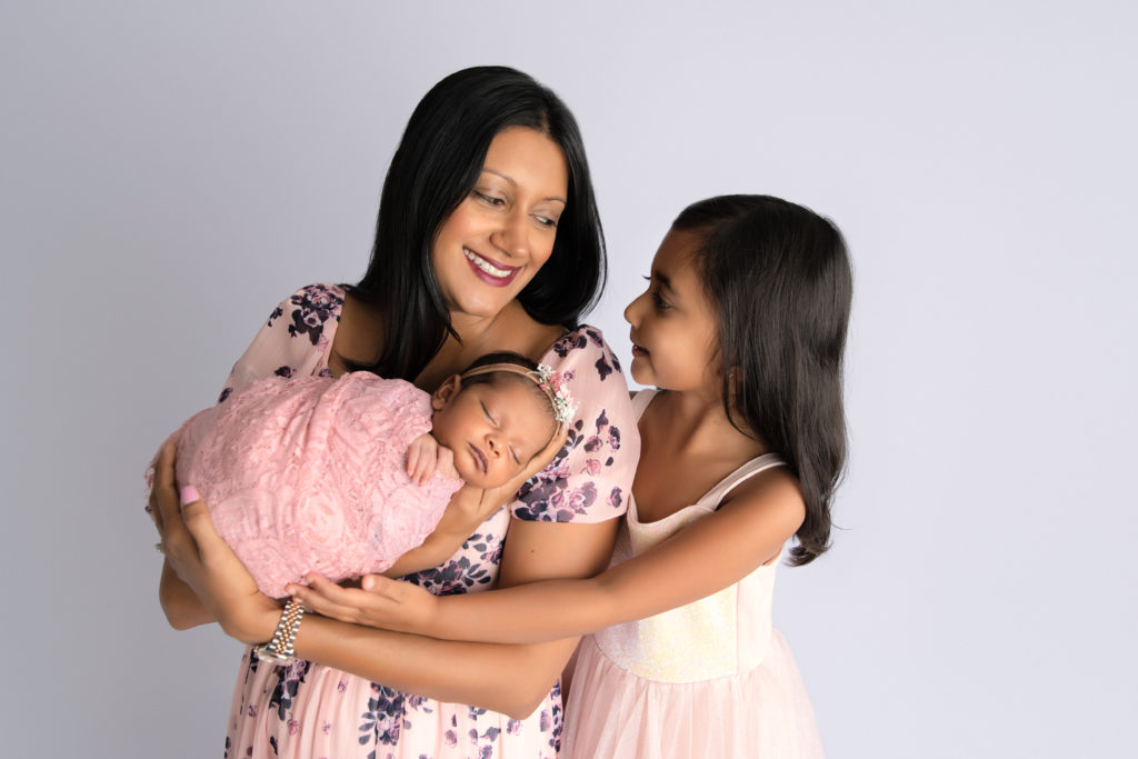 mother poses with daughter and newborn girl wrapped in pink