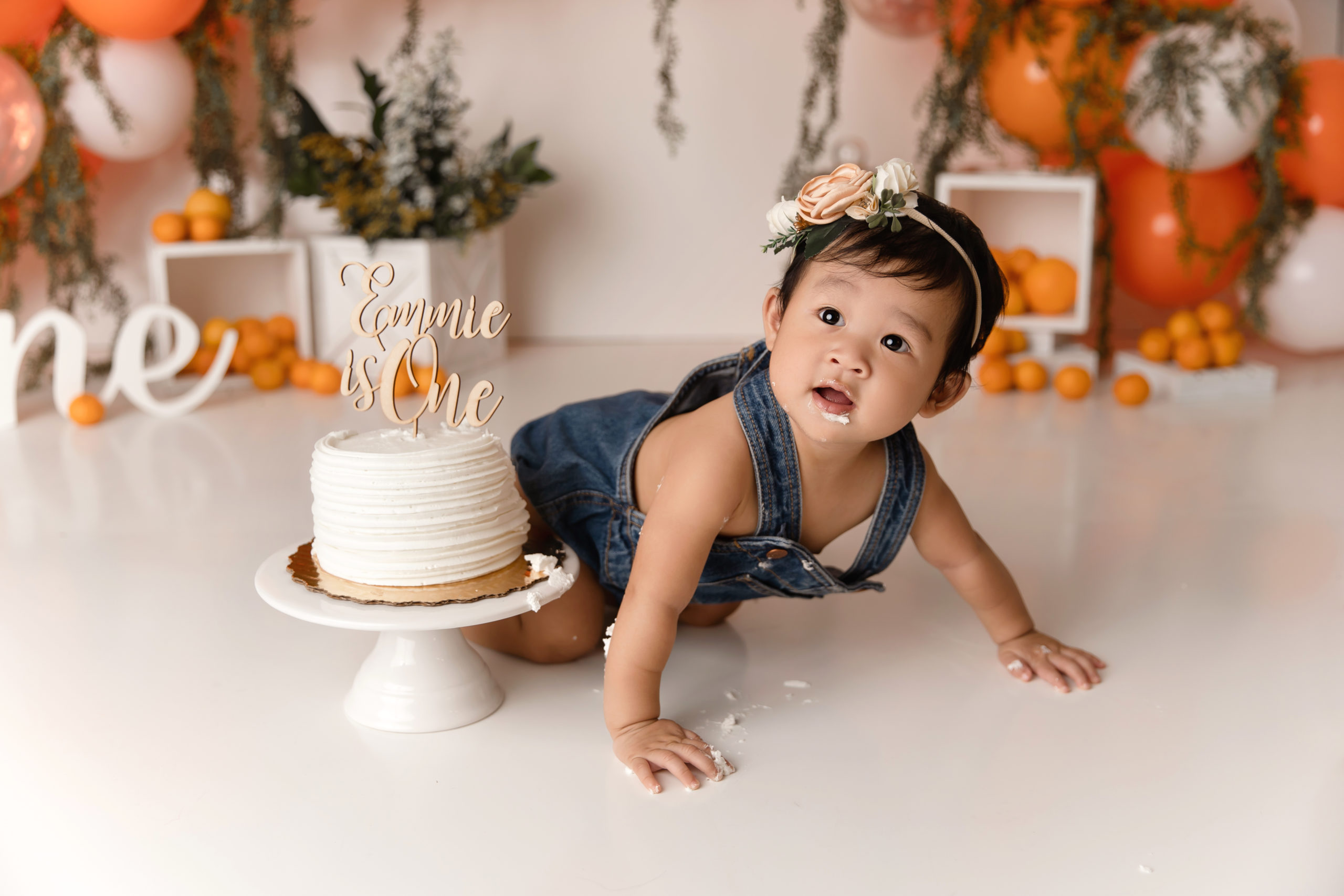 little girl in overalls crawling next to cake for birthday