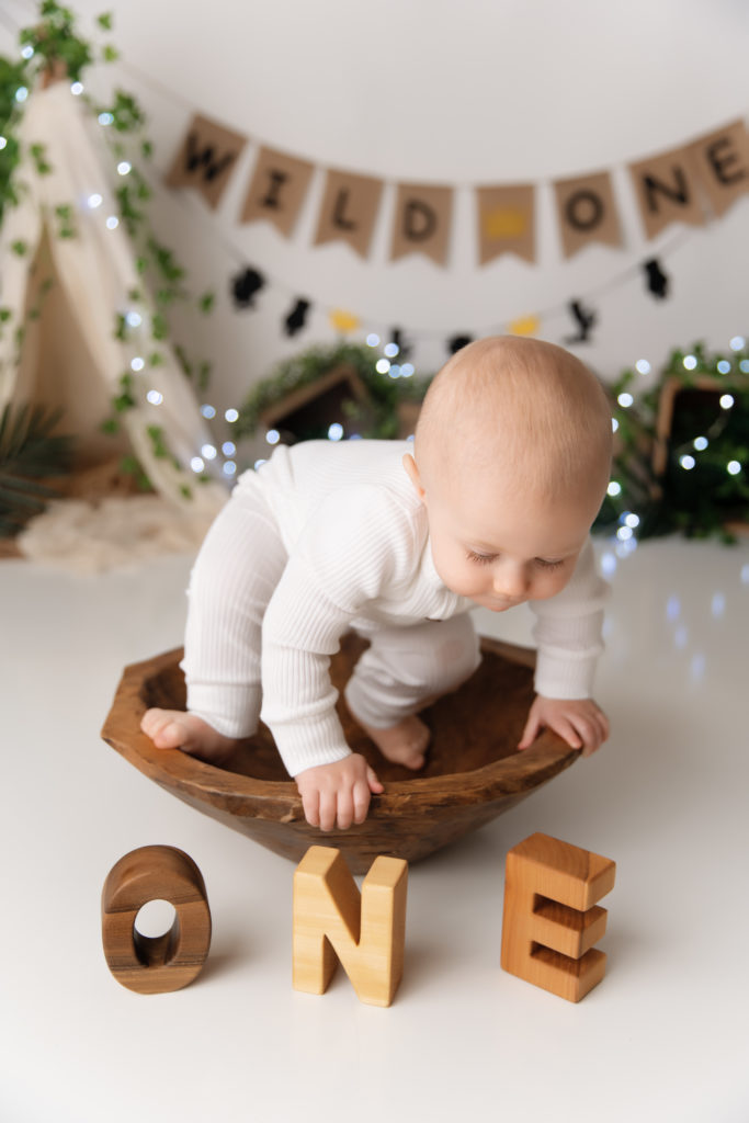 baby boy in white sits in wooden bowl overlooking one blocks