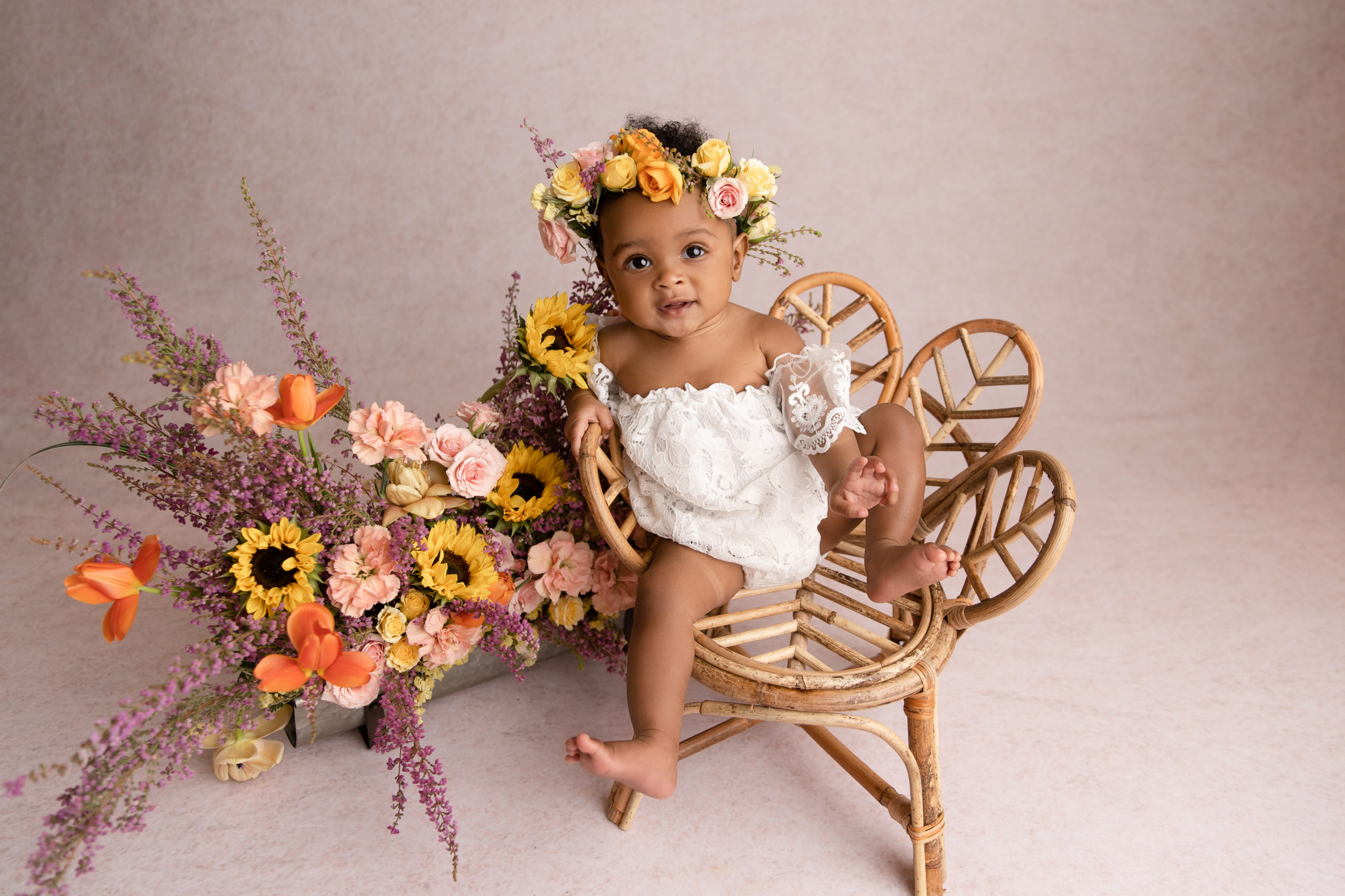 baby girl sitting in wicker chair with floral crown and matching arrangement