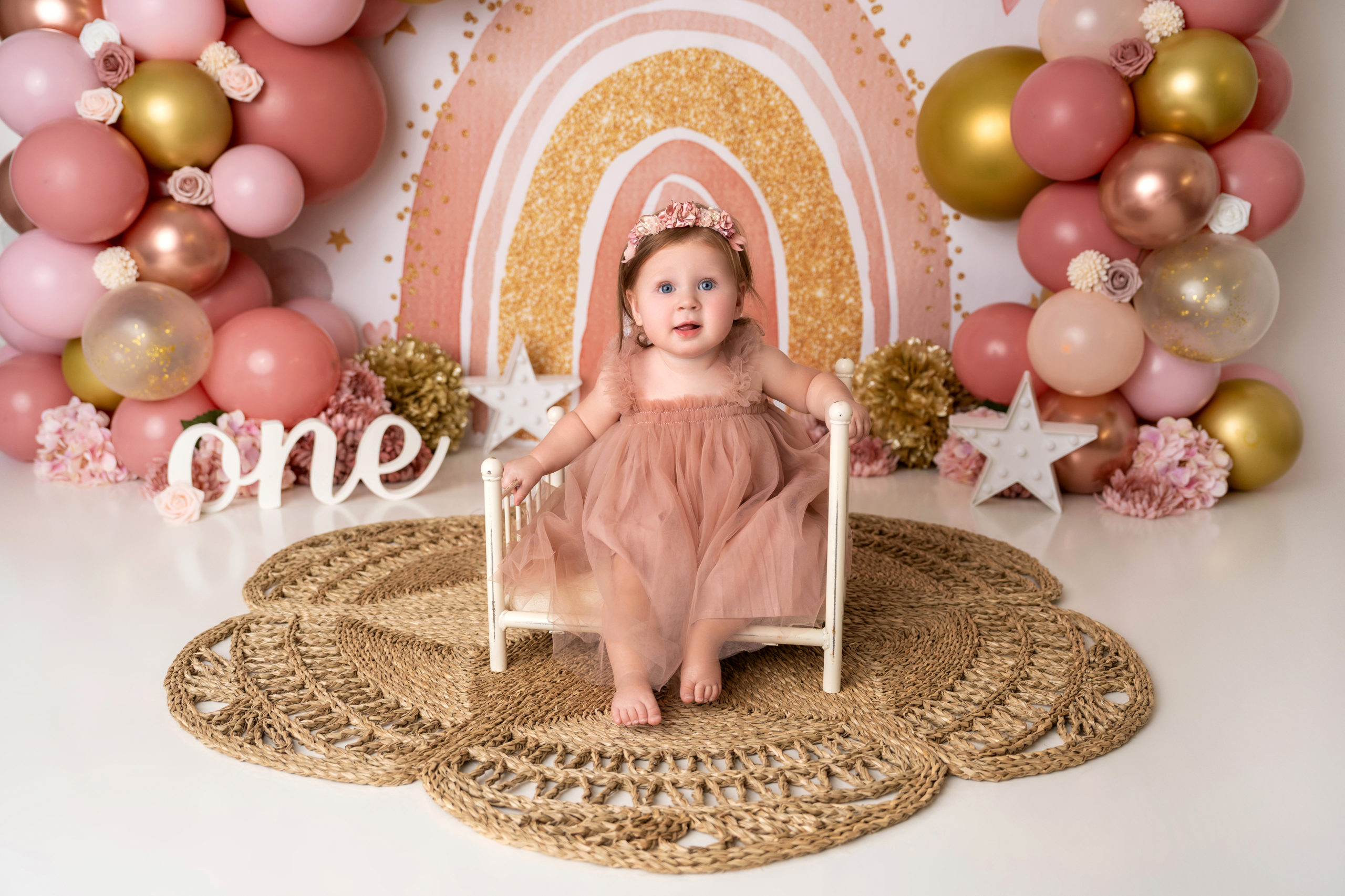 baby girl poses on white bench with pink rainbow backdrop