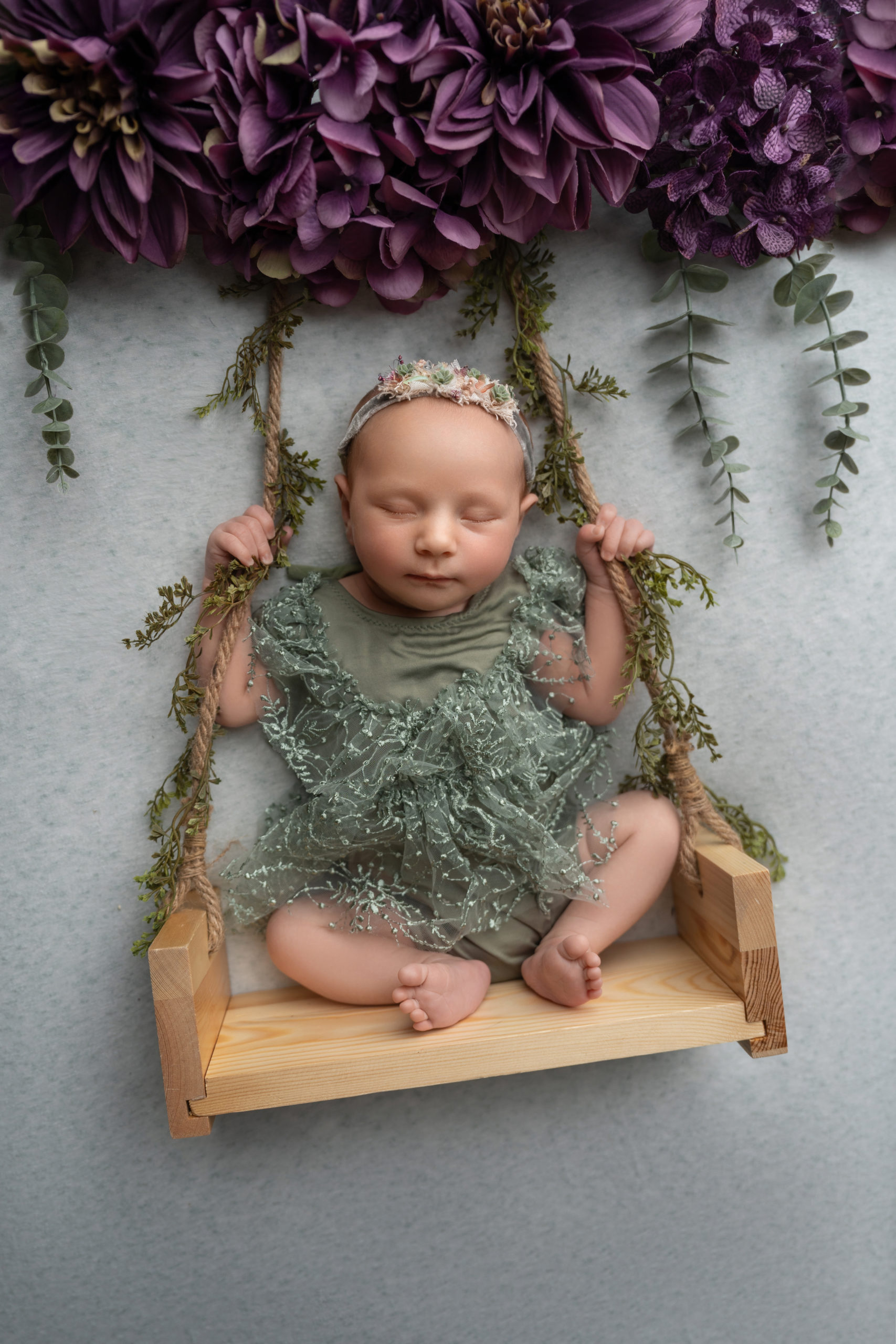 baby girl in swing prop with purple flowers above