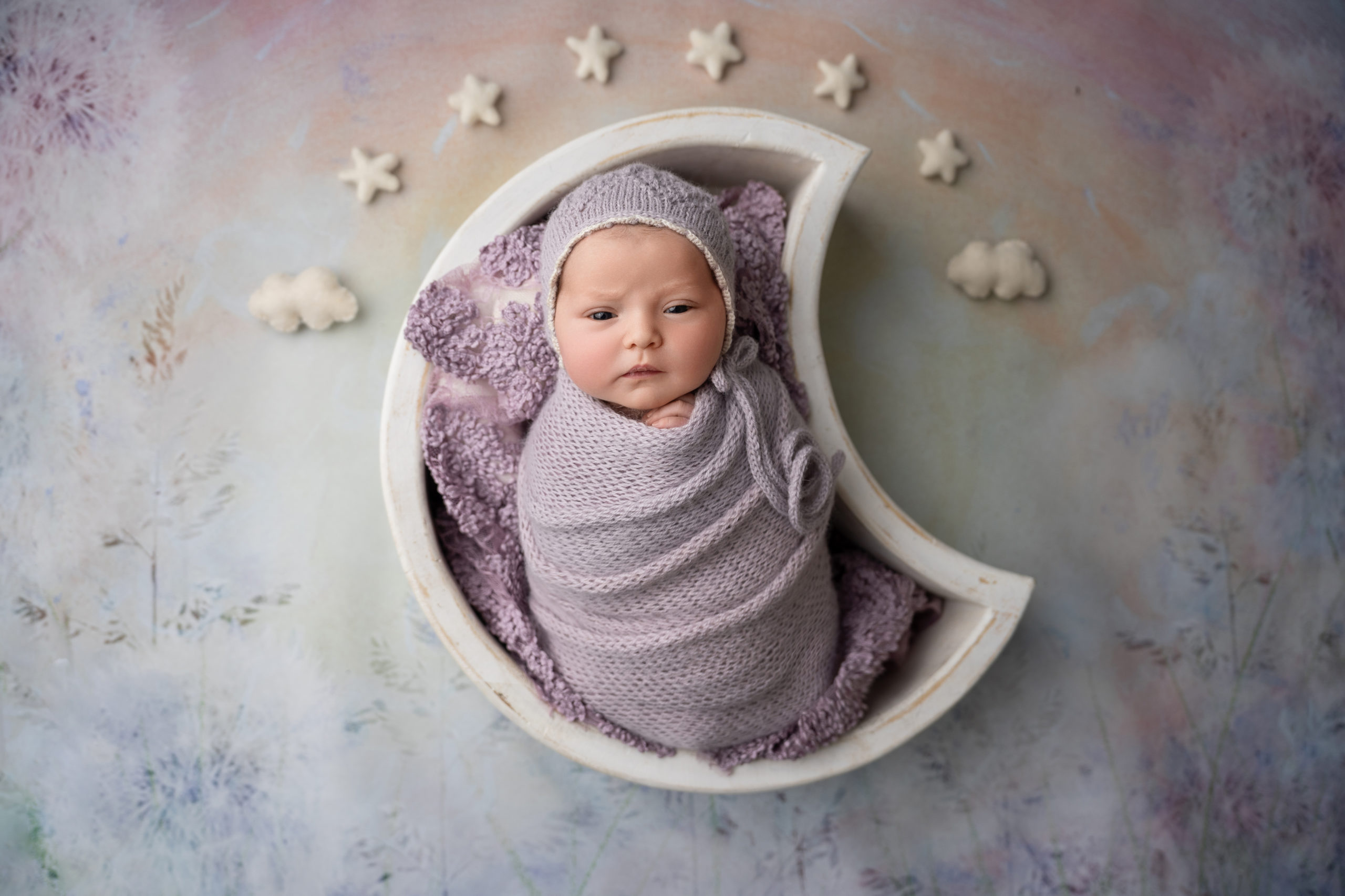 newborn girl posed in purple with matching hat in moon prop