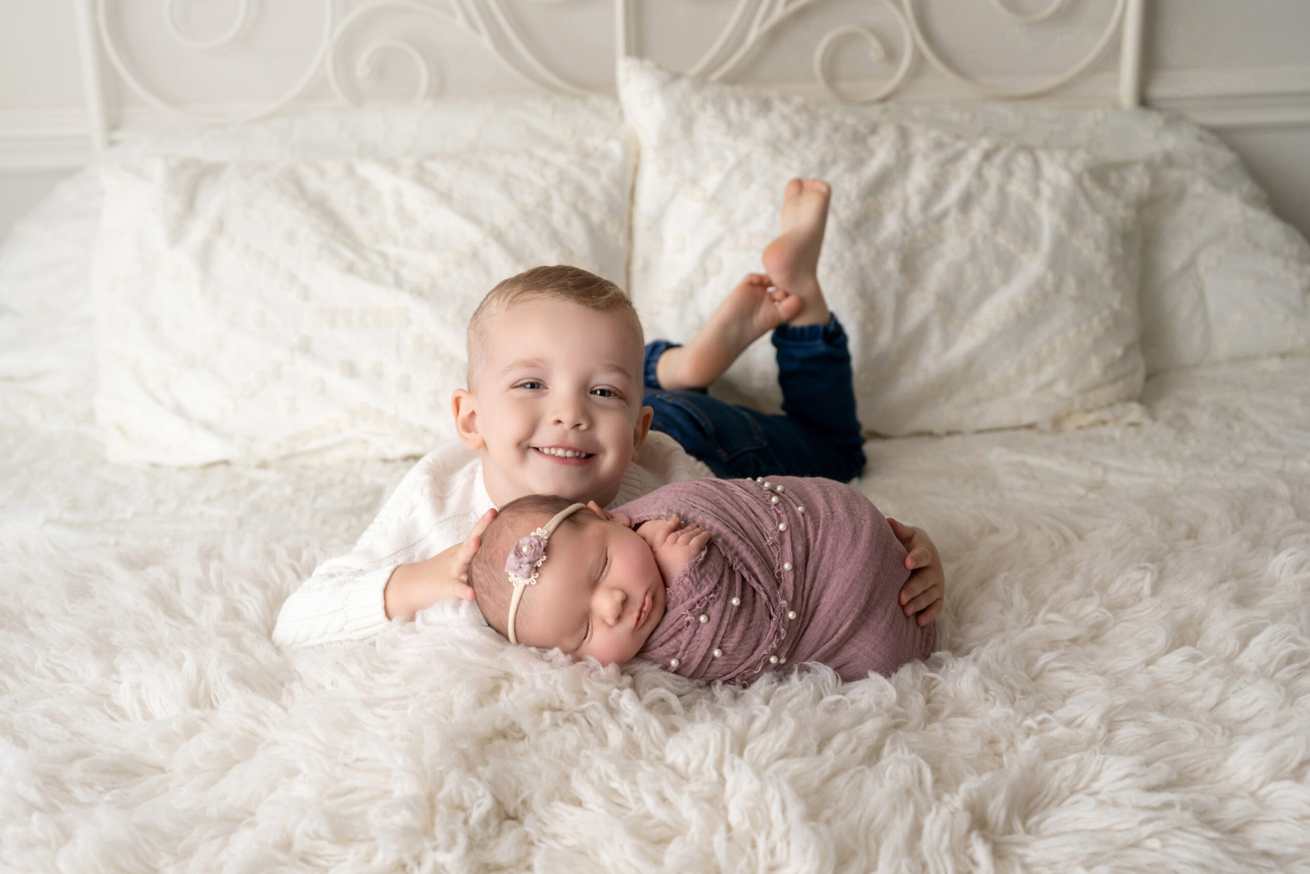 Big brother poses on bed with newborn baby sister