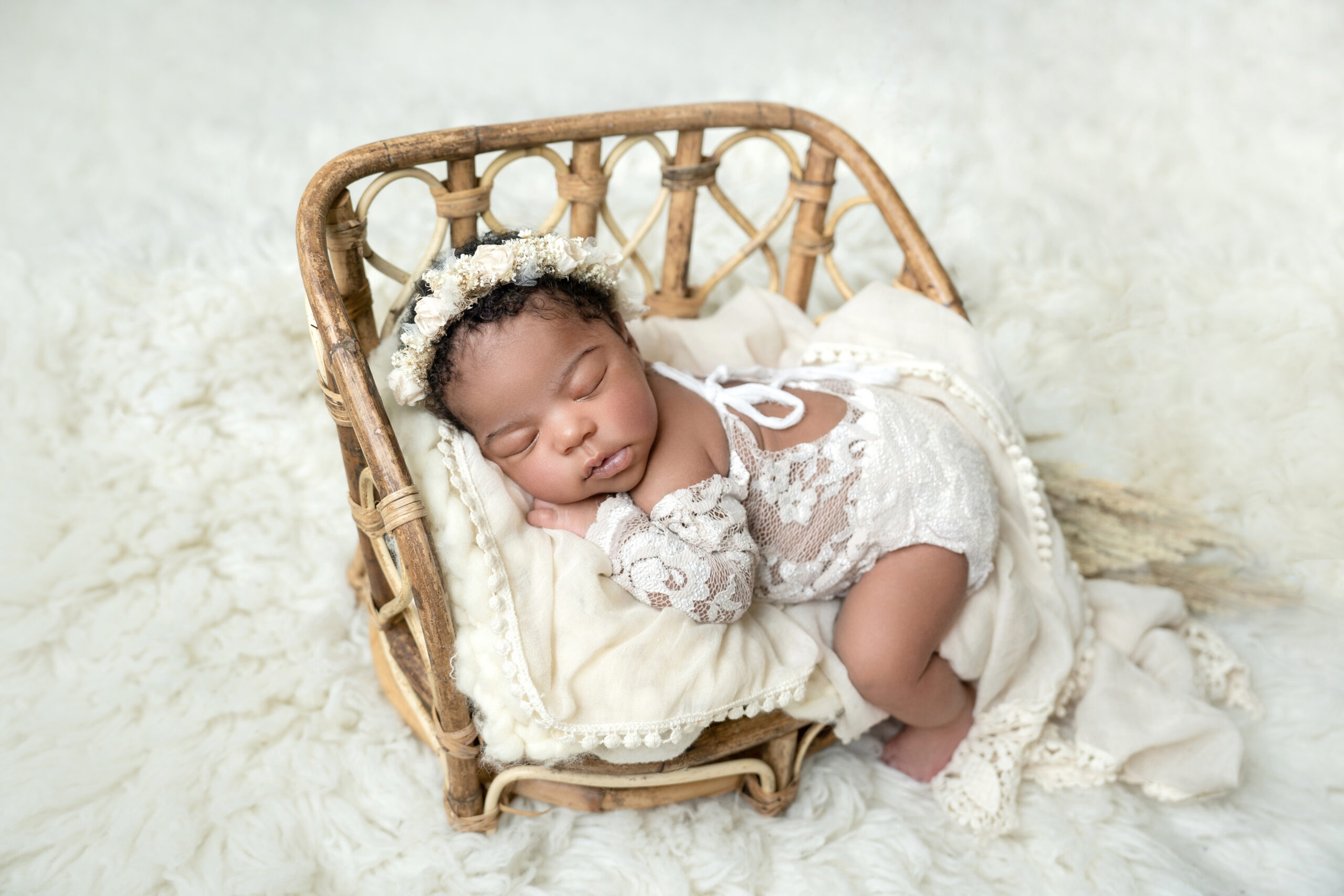 newborn girl in white lace onesie posed in wicker bed