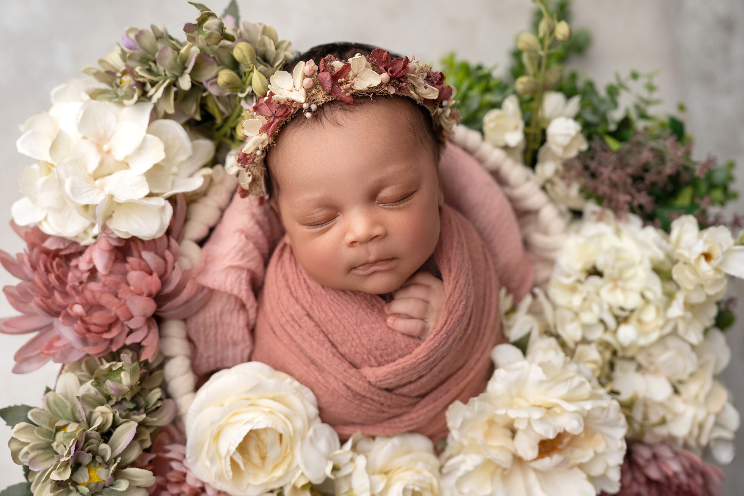 newborn girl wrapped in pink surrounded by pink and white florals