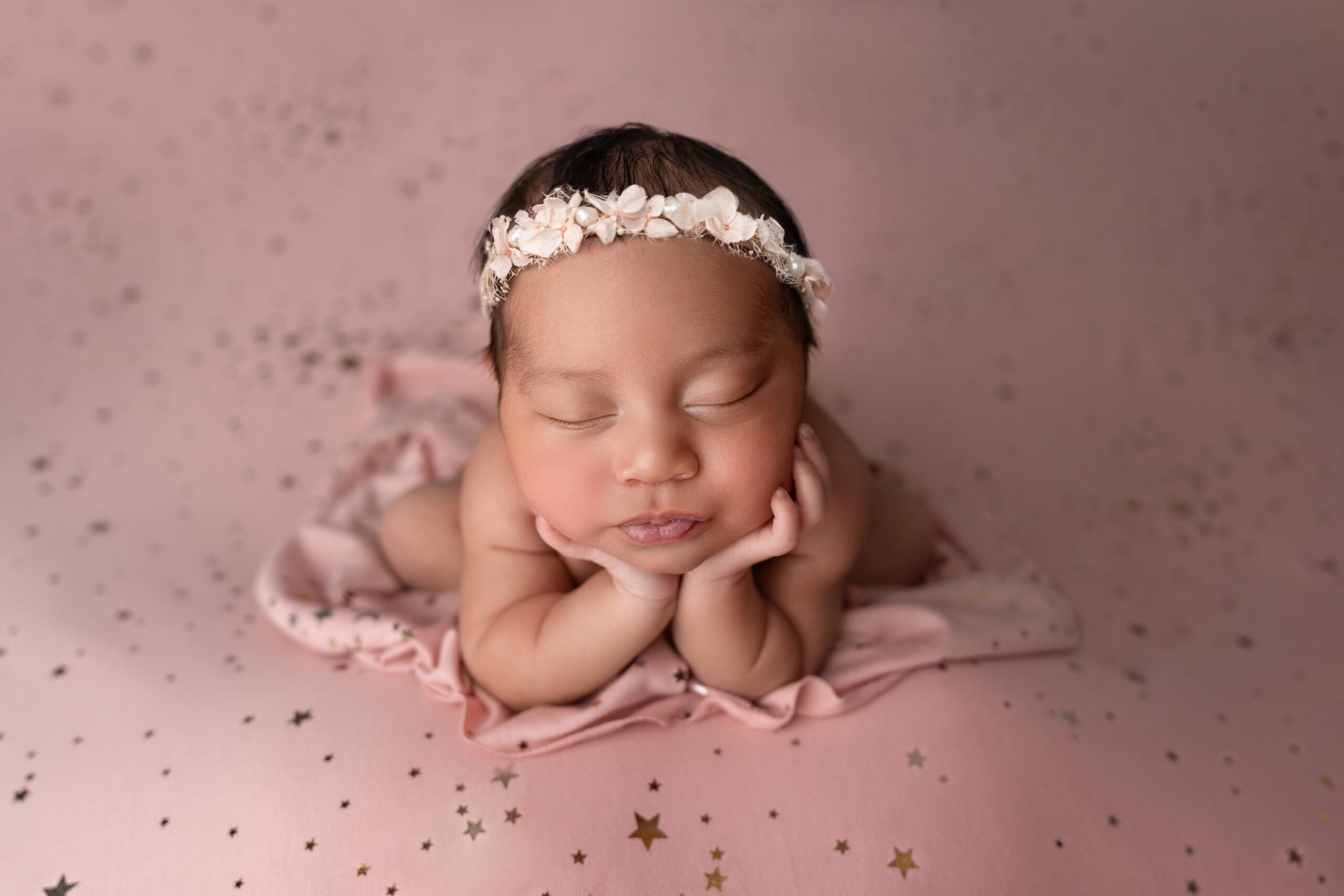 newborn girl in all pinks poses with chin on hands